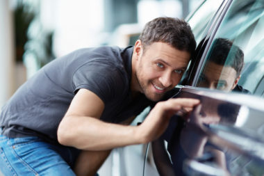 Male Driver polishing his car and smiling