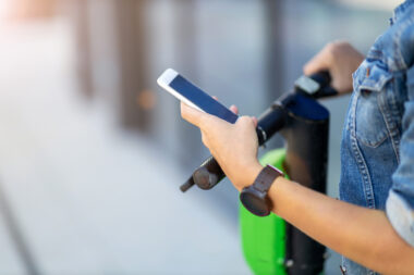 One hand on e-scooter handlebars and another holding a phone