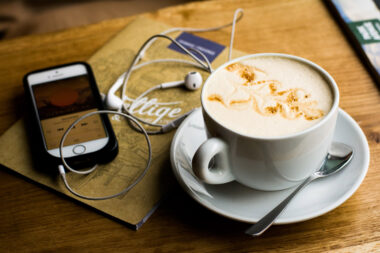 Cappuccino on a table with a phone and headphones showing a podcast playing
