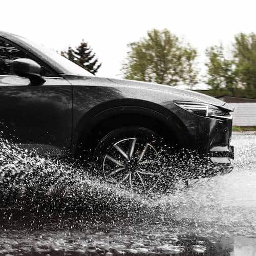 A close up of a black car driving through a puddle on the road causing a splash