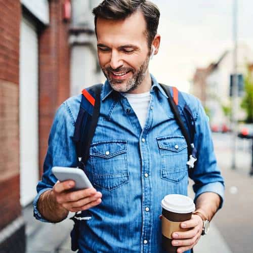 Middle aged man looking down at his phone holding a cup of coffee smiling