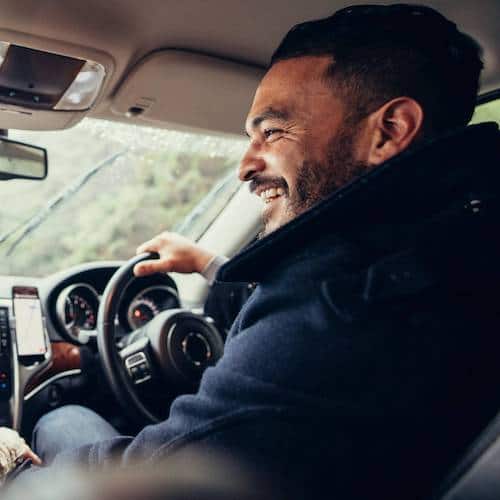 Smiling man sat behind a wheel of a modern car looking over to the passenger side