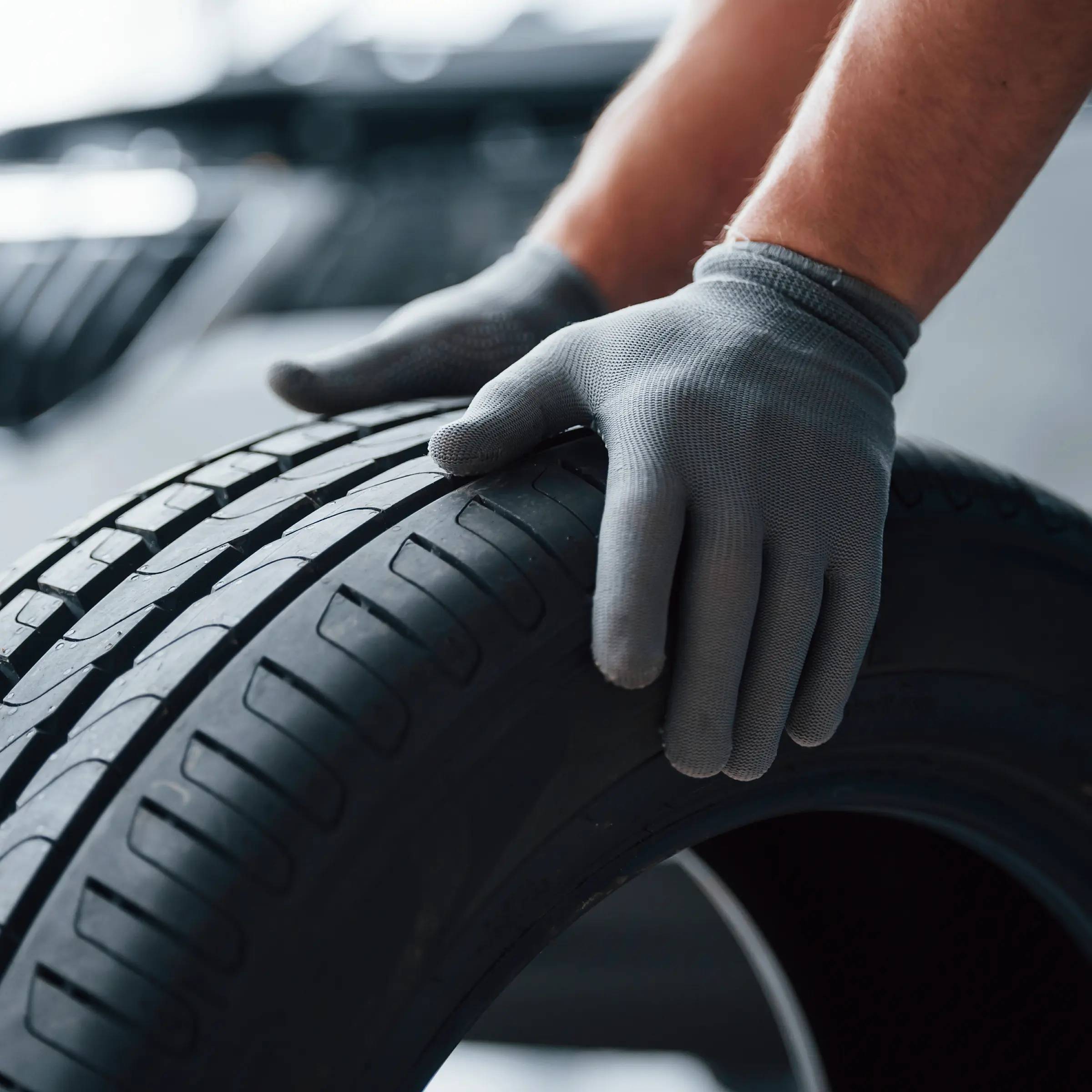 Photo of hands in grey gloves on top of a standing car tyre
