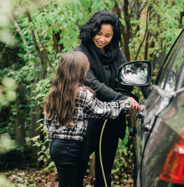 Woman with a child plugging in an electric charger to her car