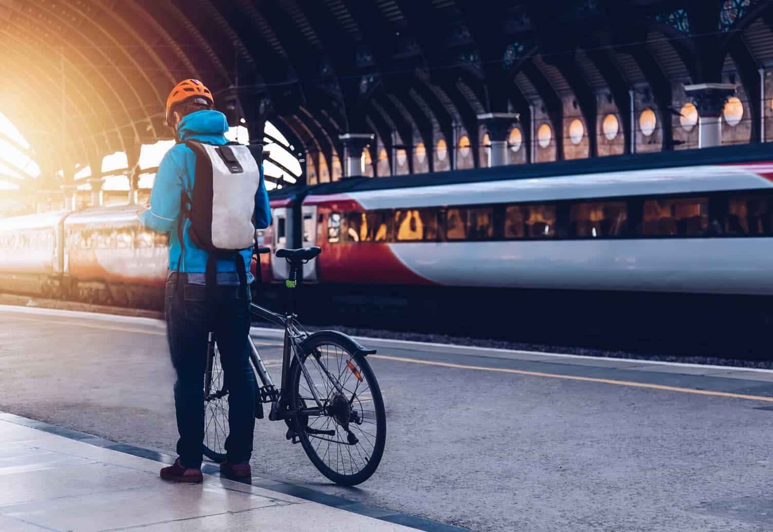 A man waiting on a train station platform with his bike, while looking at his phone or a map.