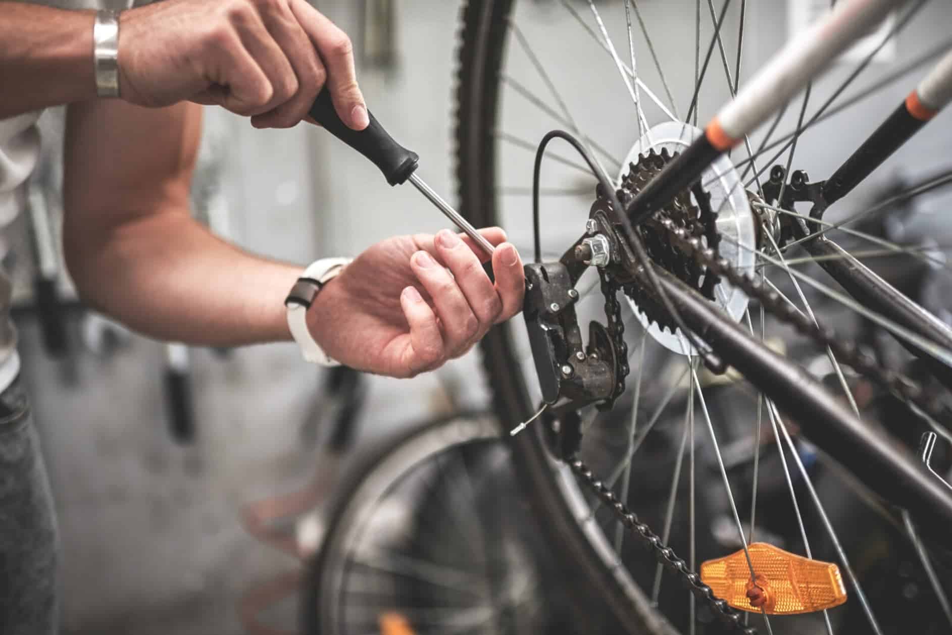 A man is fixing his rear bike wheel, he is screwing or unscrewing his chain.