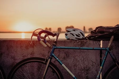 A bicycle leaded against a wall, with the sea and sunset in the background. Backpack and helmet are perched atop the wall.