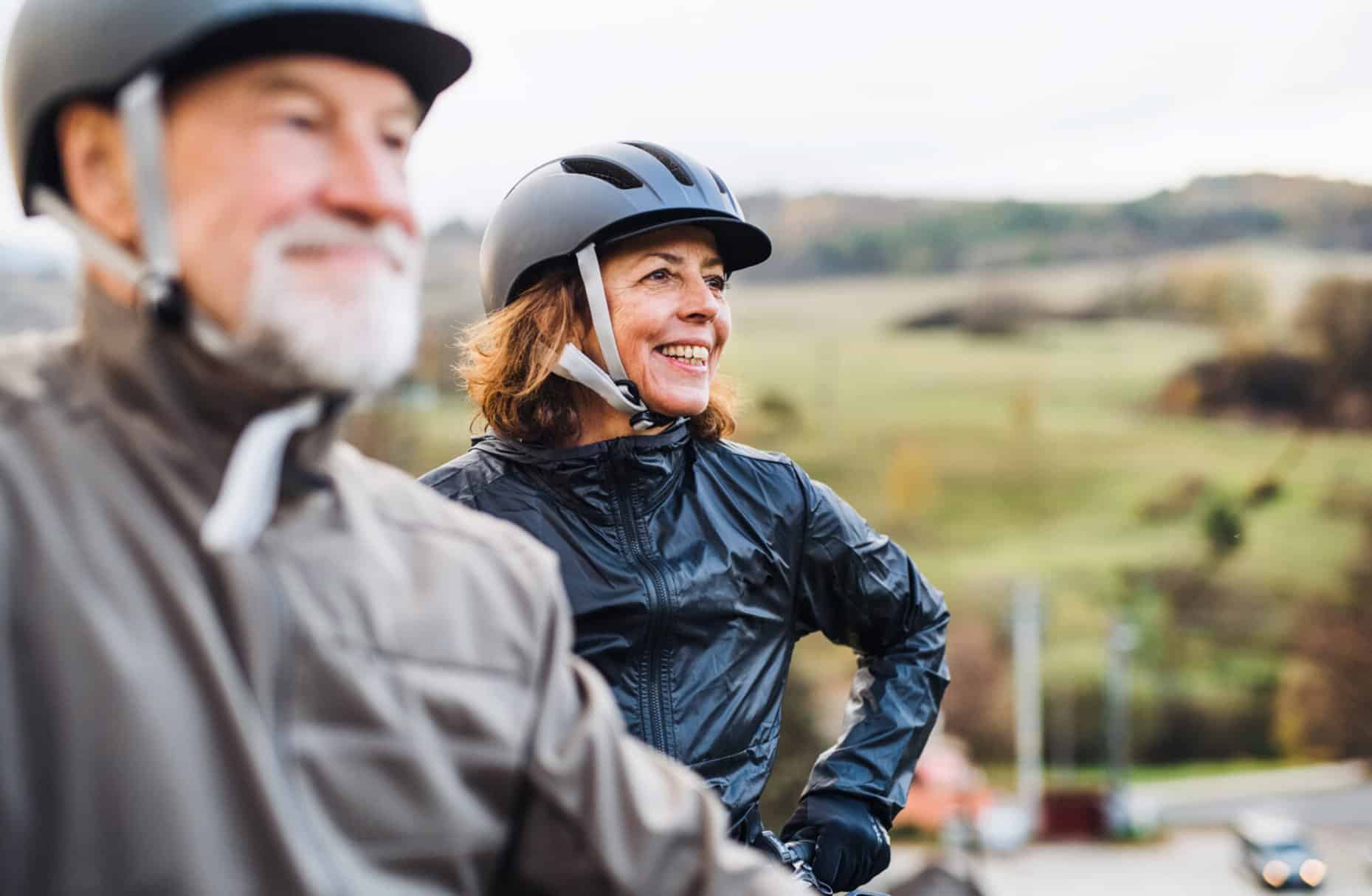 An older couple wearing bicycle helmets are looking into the distance, smiling