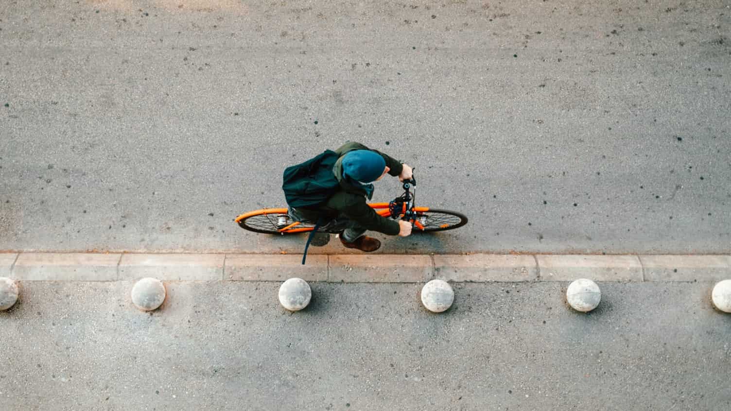 A bird-eye view of a person cycling on a concrete road, on an orange bike 