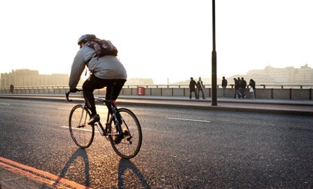 A cyclist riding along a city bridge, wearing a backpack. 