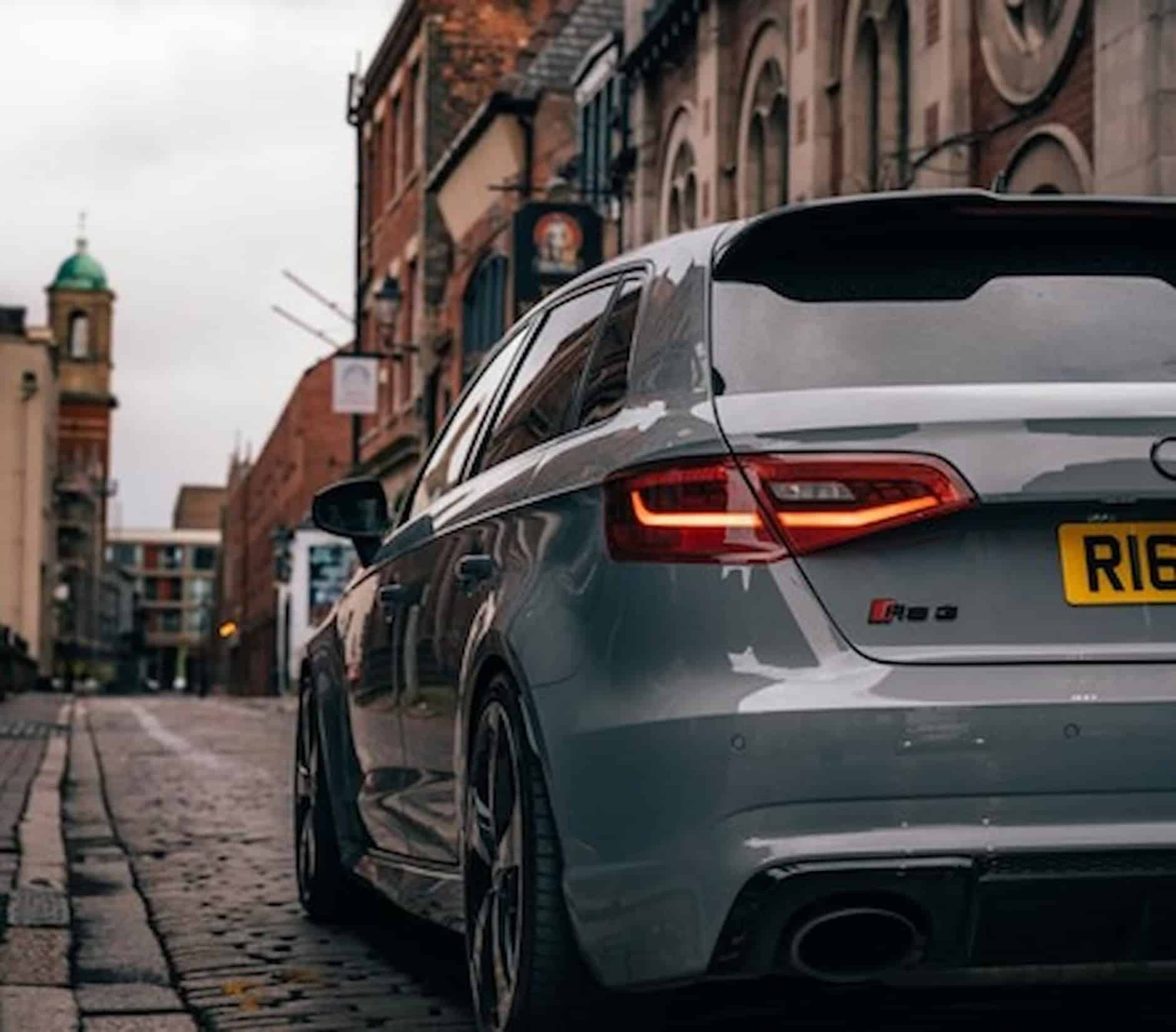 The rear end of an Audi driving along a narrow, cobbled street