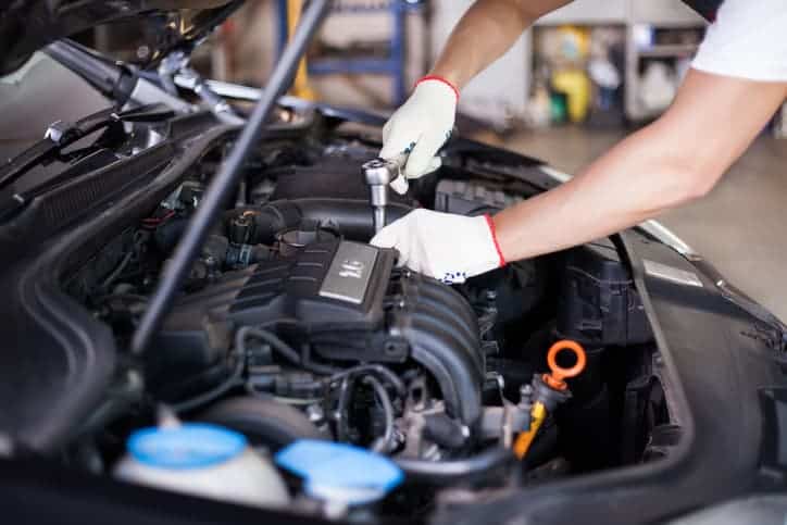 The hands of a mechanic repairing something under the bonnet of a car