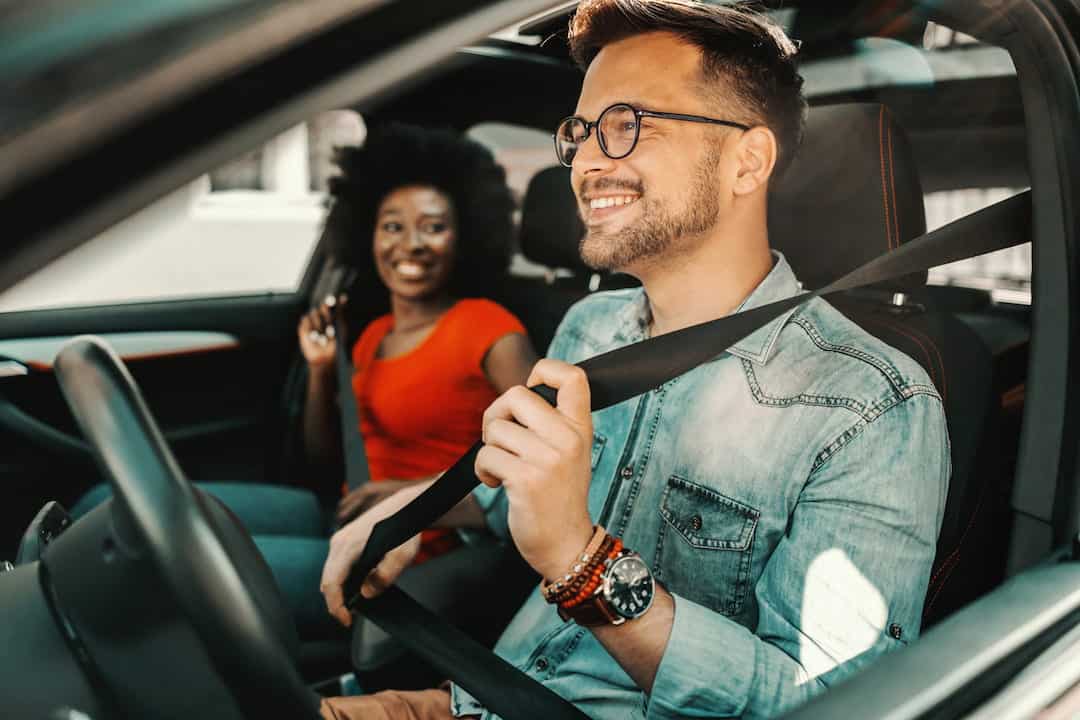 Multiracial couple in a car smiling, doing up their seatbelts