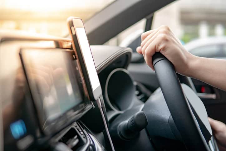 Male driver hand holding on steering wheel using smartphone for GPS navigation