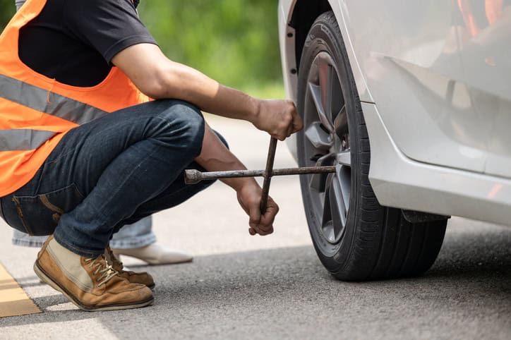 Mechanic team working road assistant help to replace flat tire service at roadside with safety reflective clothes